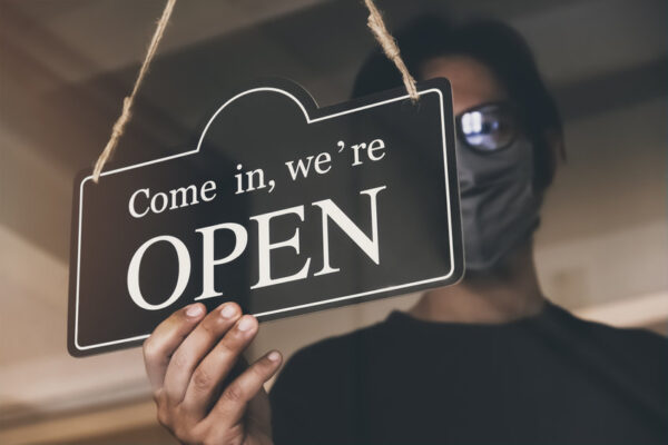 man with face mask turning an open sign on a business
